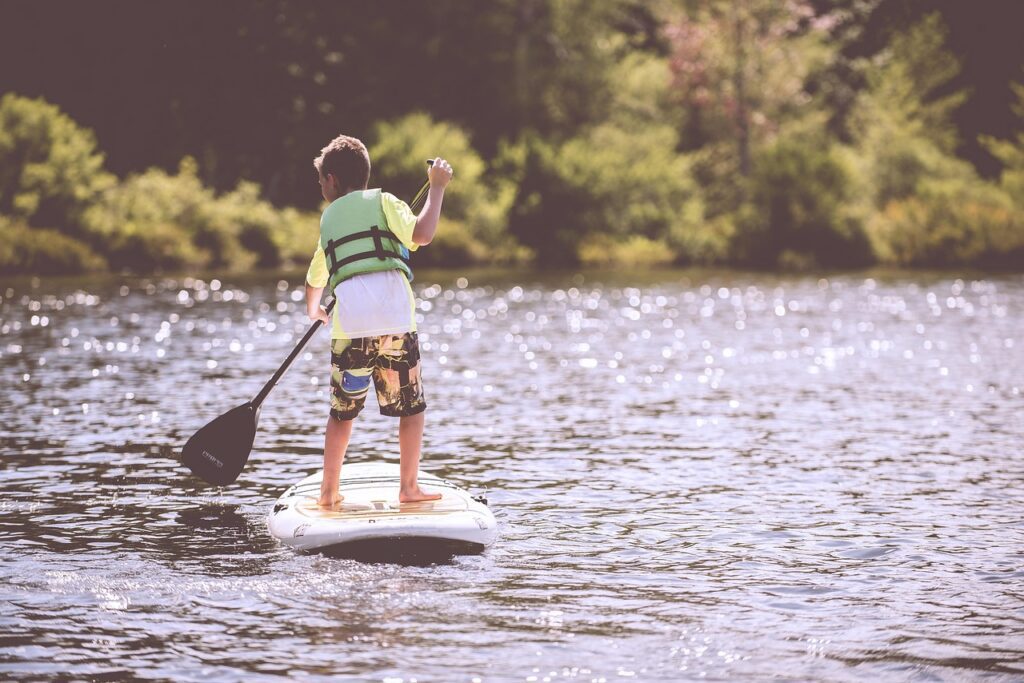 a boy in a life vest paddleboarding on a lake in Maine